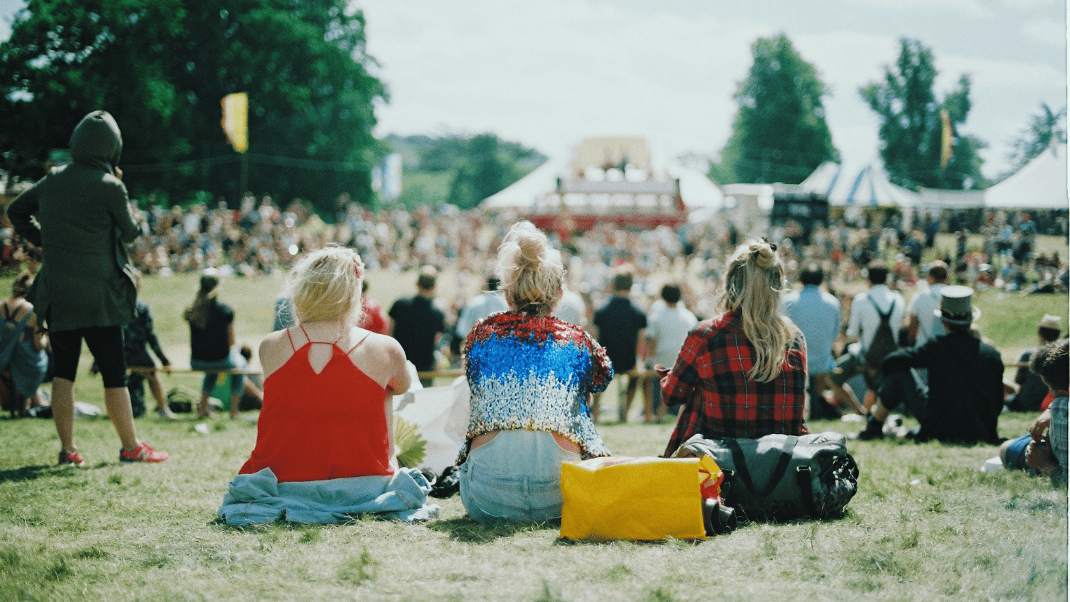 Three people sat on the grass at a festival