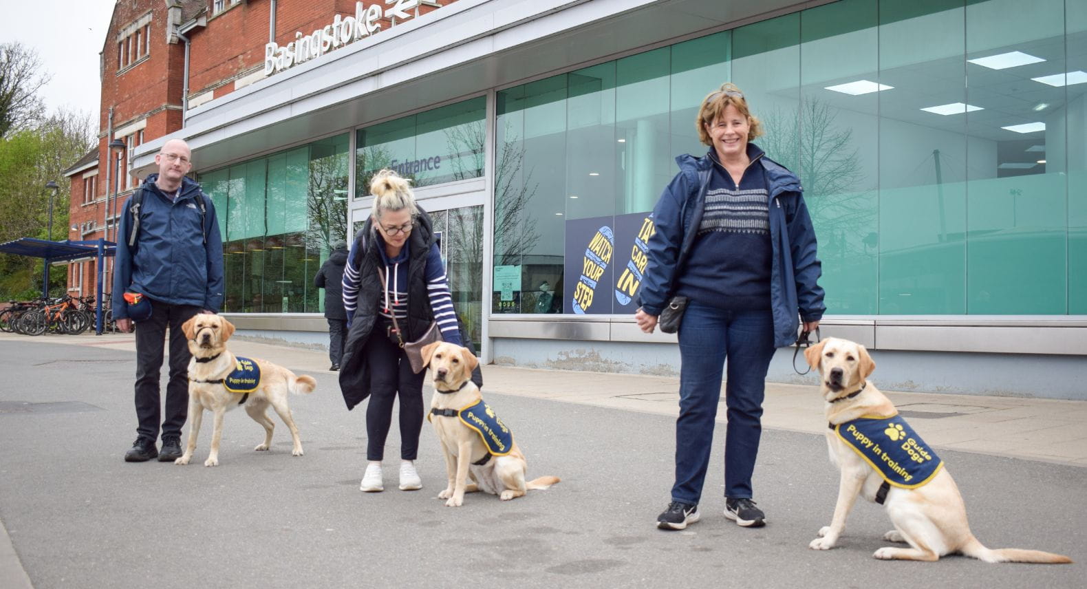 Three Guide Dog puppies and handlers lined up outside Basingstoke station