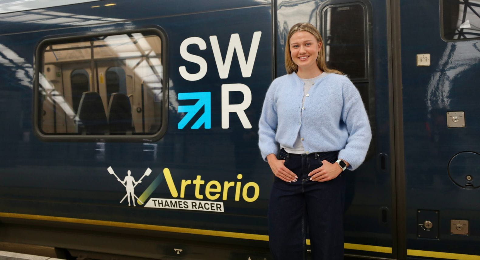Blonde woman standing beside train which says Thames Race on it