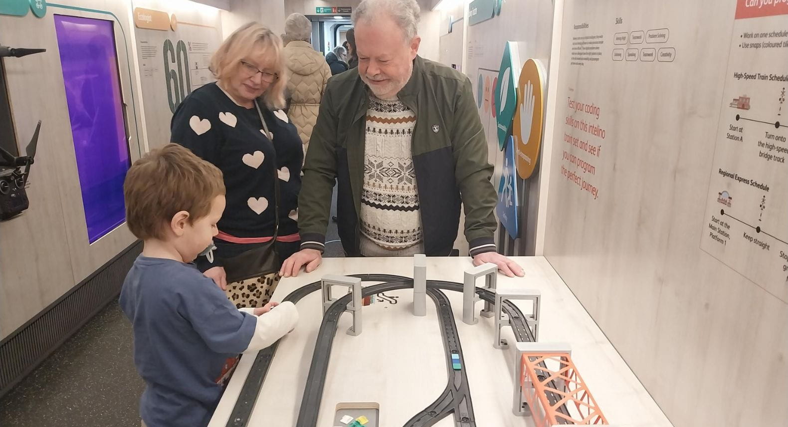 Two adults and a child in front of a railway layout diagram