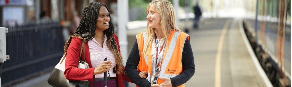 Station staff assisting person with visual impairment along platform
