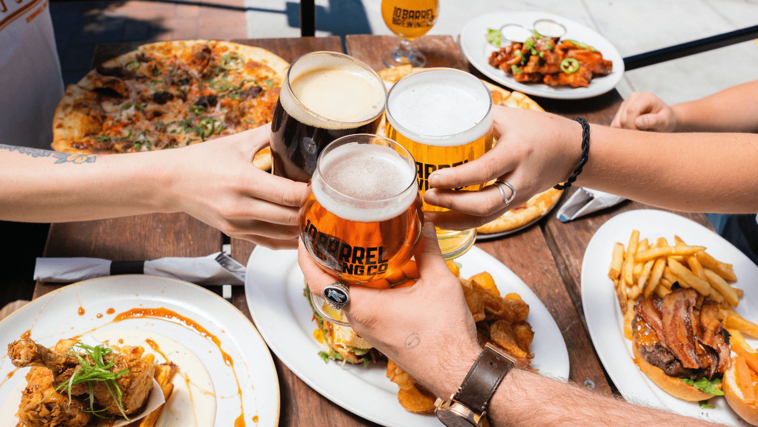 Image of people at a table cheers-ing their beers, with food on the table