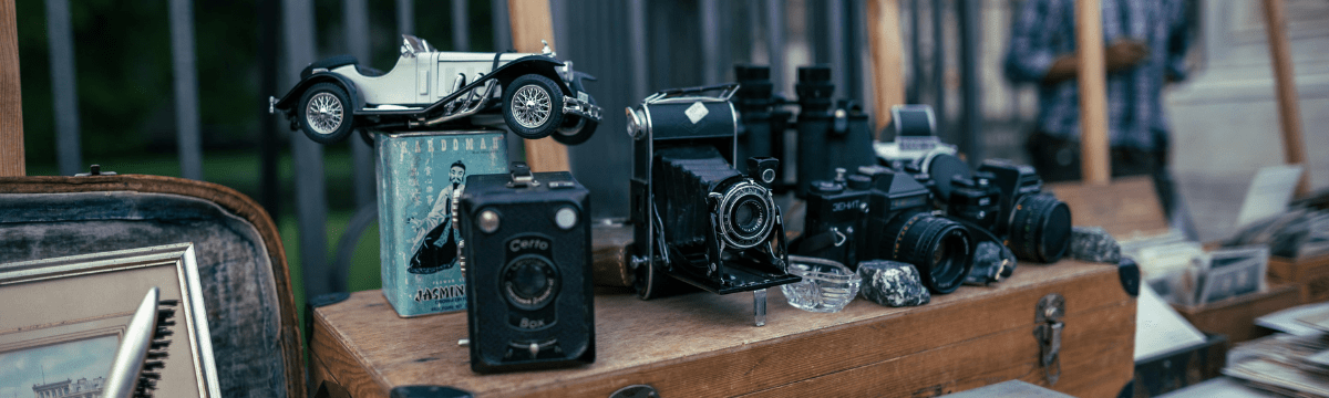Vintage cameras and small antiques displayed on a wooden table at an outdoor market.