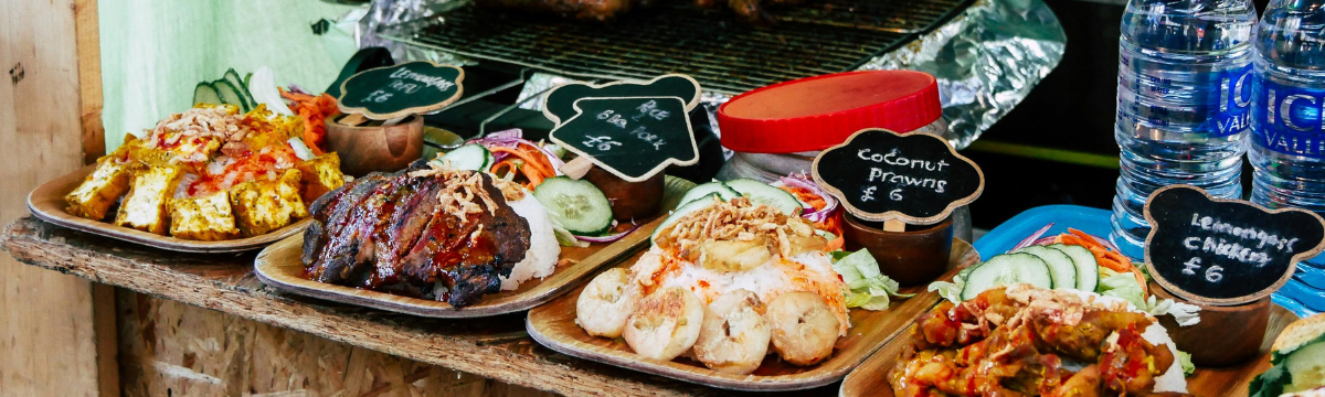 A street‑food counter showing dishes of tofu, prawns, and chicken beside a grill.