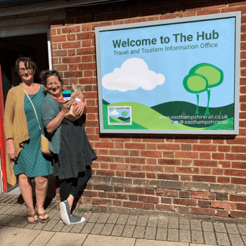 2 women smiling in front of a sign